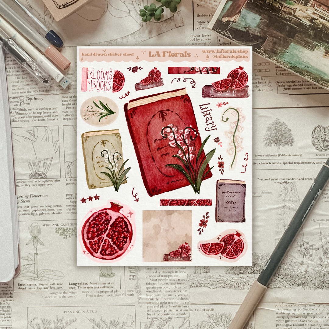 A sticker sheet showing illustrations of books and flowers and fruit sits on a textured surface with stationery items. 
